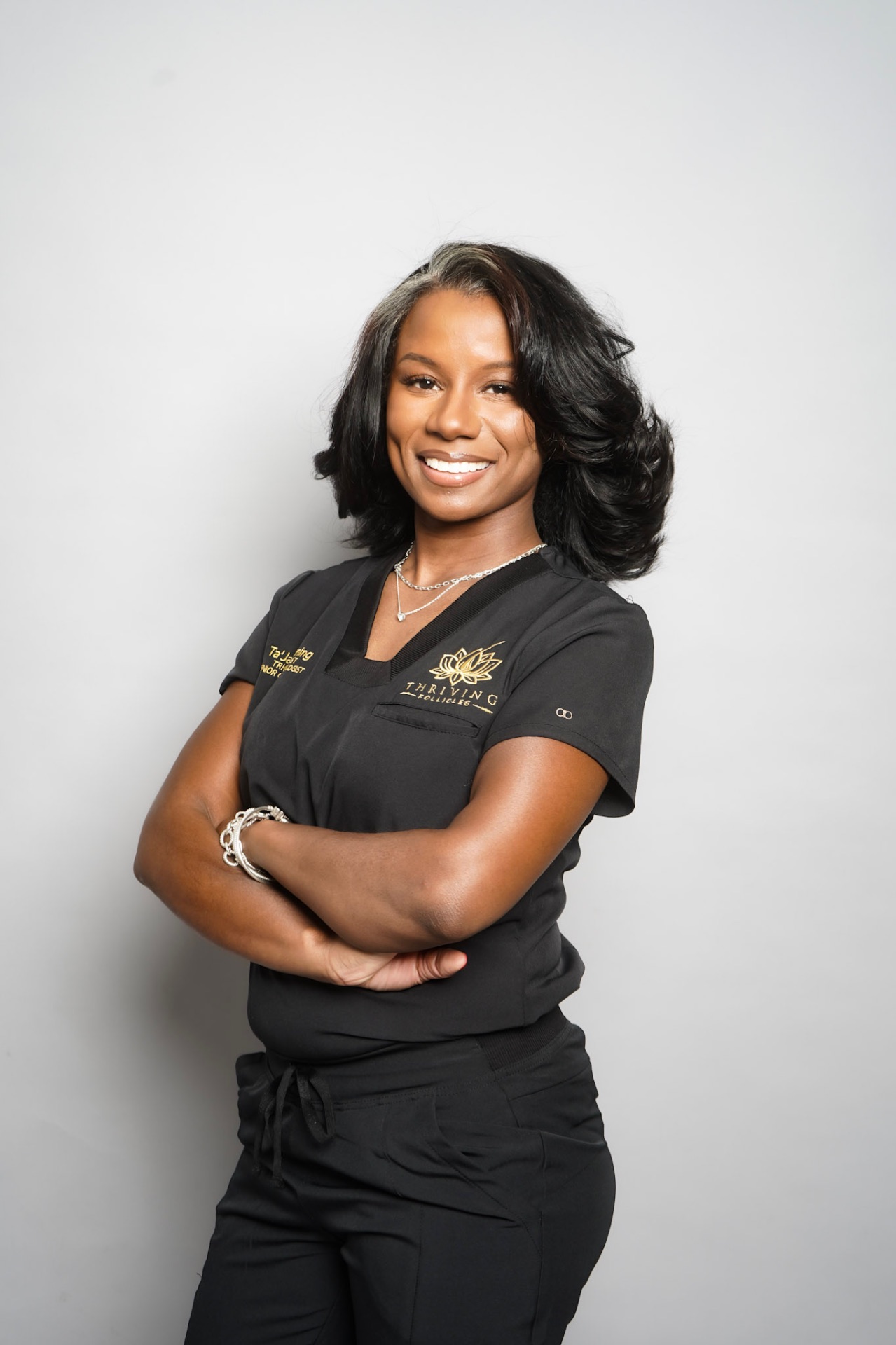 Ta’Jah Fleming in black Thriving Follicles scrubs with the gold lotus mark